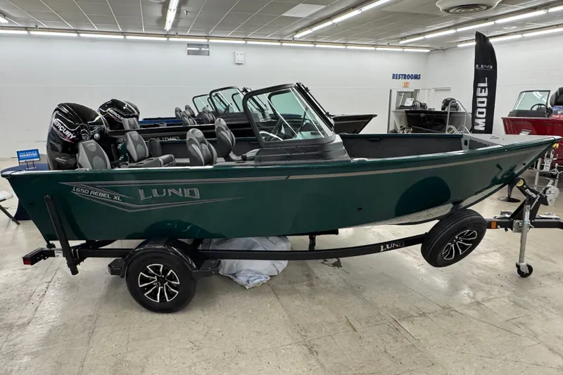 Slide: The Image of 2026 Lund 1650 Rebel XL Sport boat displayed indoors on a trailer. - 1