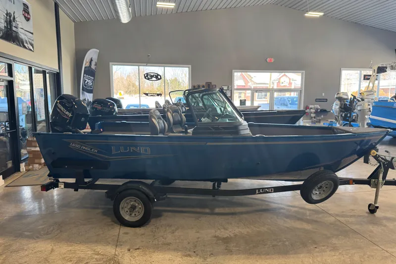 Slide: The Image of 2026 Lund 1650 Angler Sport boat displayed in showroom on trailer. - 2