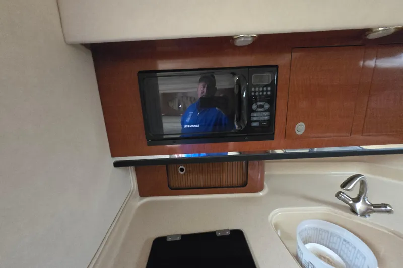 Slide: The Image of 2005 Sea Ray 290 Amberjack interior with microwave, sink, and wooden cabinetry. - 28
