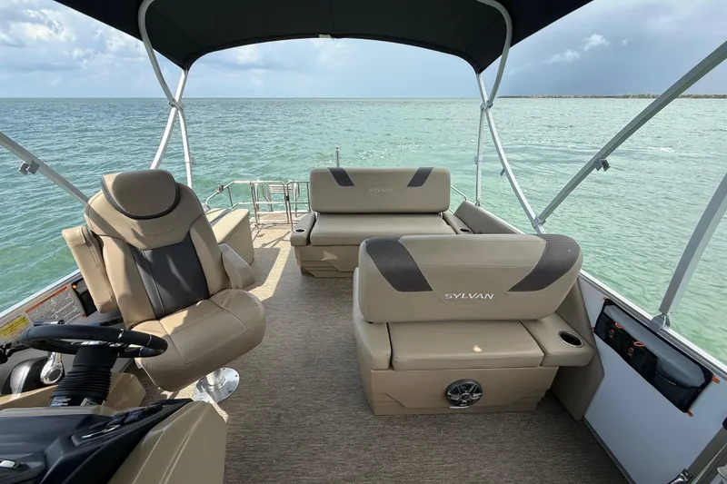 Slide: The Image of 2021 Sylvan L1 SPX boat interior with beige seating, steering console, and canopy on open water. - 14