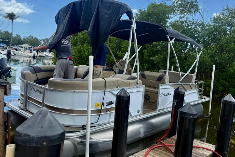 Slide: The Image of 2021 Sylvan L1 SPX pontoon boat docked, featuring canopy and seating, surrounded by lush greenery. - 22