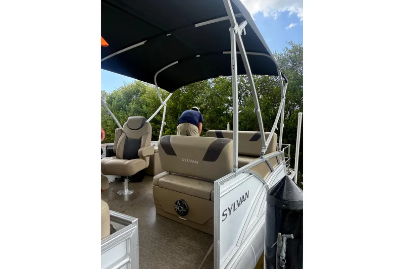 Slide: The Image of 2021 Sylvan L1 SPX pontoon boat interior with seating and canopy, docked near greenery. - 24
