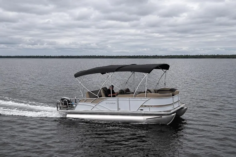 Slide: The Image of 2021 Sylvan L1 SPX pontoon boat cruising on a calm lake under cloudy skies. - 4