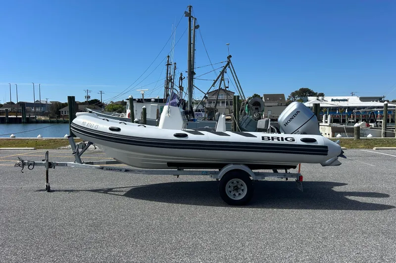 The Image of 2016 Brig Navigator 520 inflatable boat on trailer, parked near marina under clear blue sky. - 0