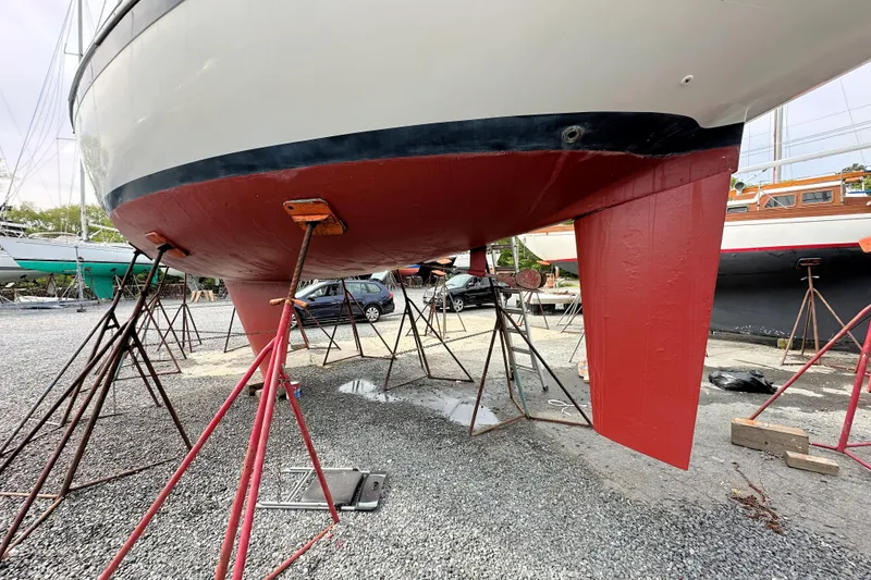 Slide: The Image of 1991 Ericson 380 sailboat on stands, showcasing red-painted hull and keel in a boatyard. - 24
