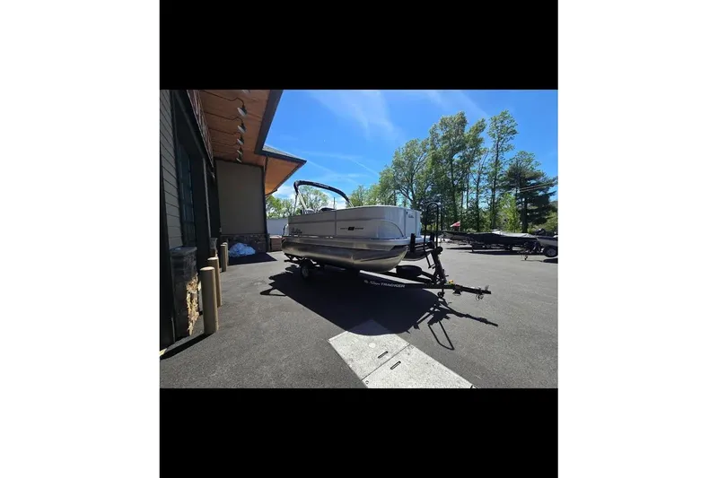 Slide: The Image of 2026 Sun Tracker Party Barge 16 DLX on trailer, parked outdoors under clear blue sky. - 2