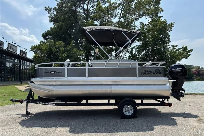 The Image of 2026 Sun Tracker Bass Buggy 18 DLX pontoon boat on trailer, parked near a lake. - 0