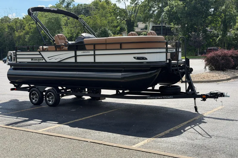 Slide: The Image of 2026 Ranger 223FC pontoon boat on trailer in parking lot, surrounded by trees. - 8