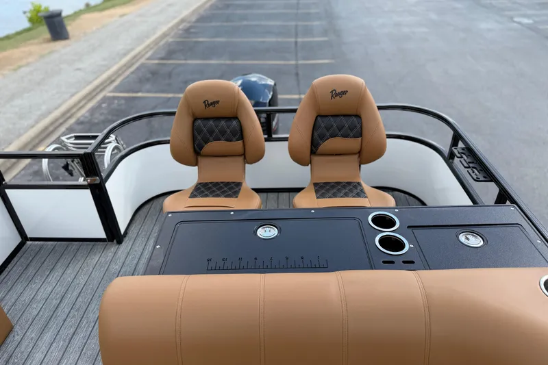 Slide: The Image of 2026 Ranger 223FC boat interior with tan seats and black console, parked by a lakeside. - 19