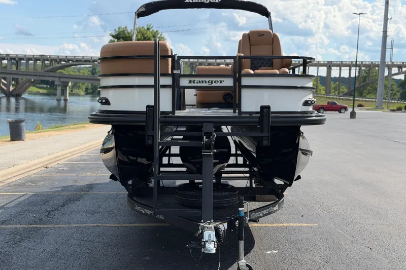 Slide: The Image of 2026 Ranger 223FC pontoon boat on trailer, parked near a scenic river and bridge. - 9