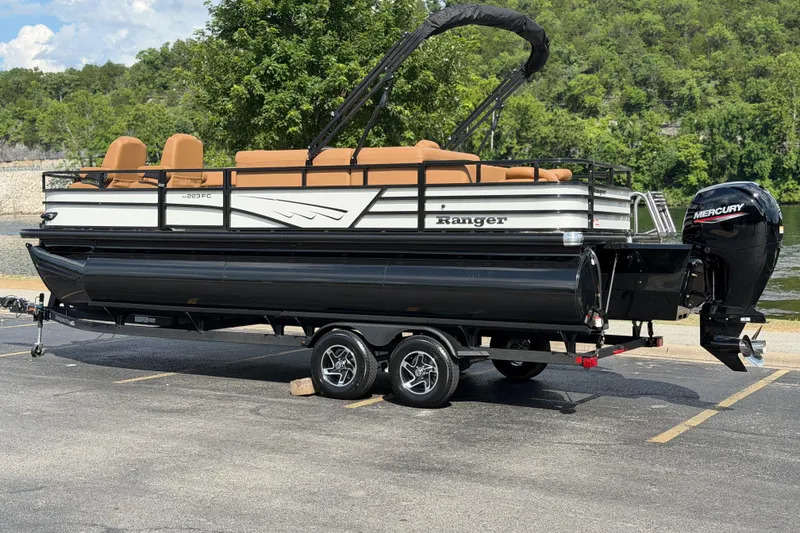 Slide: The Image of 2026 Ranger 223FC pontoon boat on trailer, parked by a scenic lake. - 1