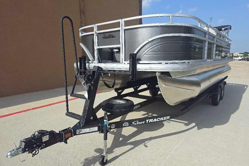 Slide: The Image of 2026 Sun Tracker Fishin' Barge 20 DLX pontoon boat on trailer, parked outdoors. - 2
