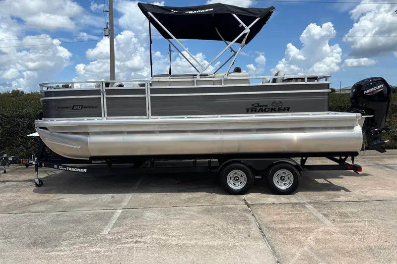 The Image of 2026 Sun Tracker Fishin' Barge 20 DLX pontoon boat on trailer under blue sky. - 0