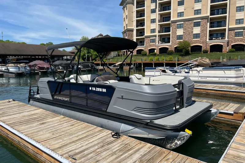 The Image of 2026 Starcraft GX 22 R DH pontoon boat docked at marina with modern buildings. - 0