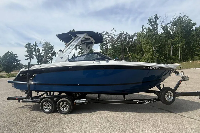 The Image of 2024 Cobalt R8 Surf boat on trailer, blue hull, parked outdoors. - 1