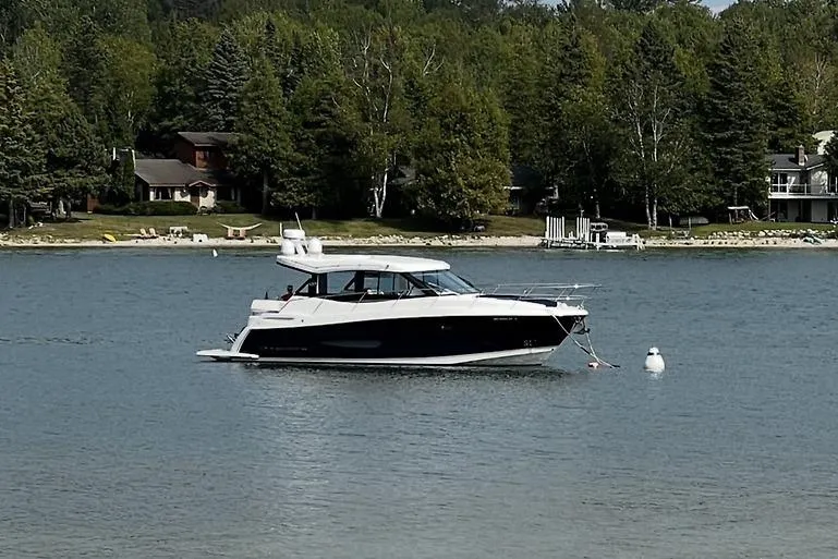 The Image of 2024 Regal 38 Grande Coupe yacht on a serene lake with lush green shoreline. - 1