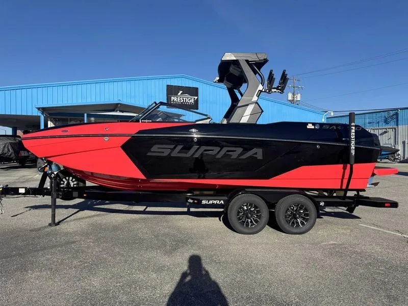 The Image of 2025 Supra SA boat in red and black on a trailer, parked outside a blue building. - 0