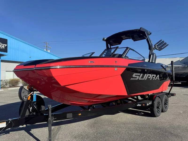 Slide: The Image of 2025 Supra SA boat in vibrant red on a trailer, parked outdoors. - 2