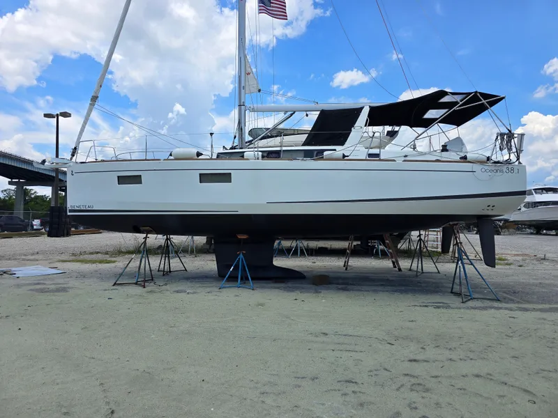 Slide: The Image of A 2023 Beneteau Oceanis 38.1 sailboat is on stands on land under a cloudy sky. - 24