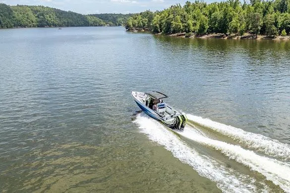 Slide: The Image of 2024 Sunsation 32 CCX boat cruising on a scenic lake with lush green shoreline. - 17