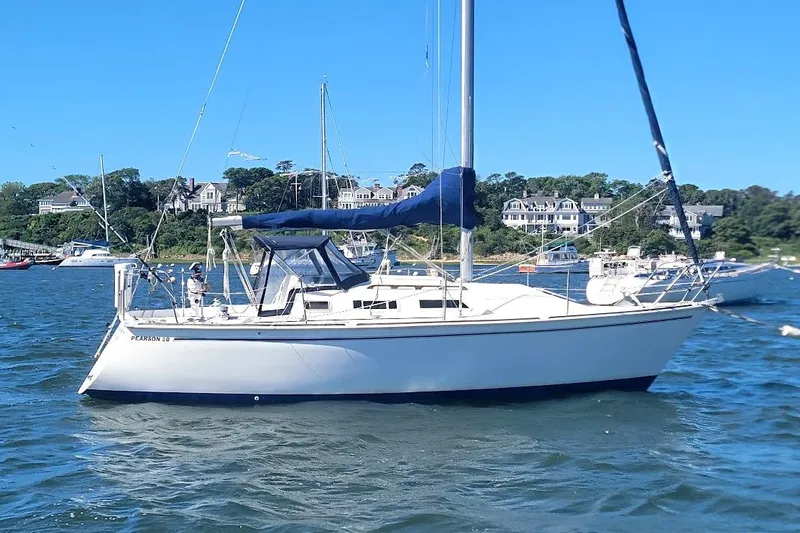 The Image of 1986 Pearson 28 sailboat anchored in scenic harbor with coastal homes in background. - 2