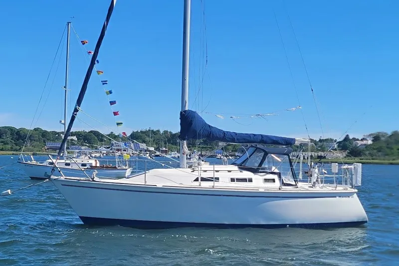 Slide: The Image of 1986 Pearson 28 sailboat anchored in a scenic harbor with colorful flags. - 23