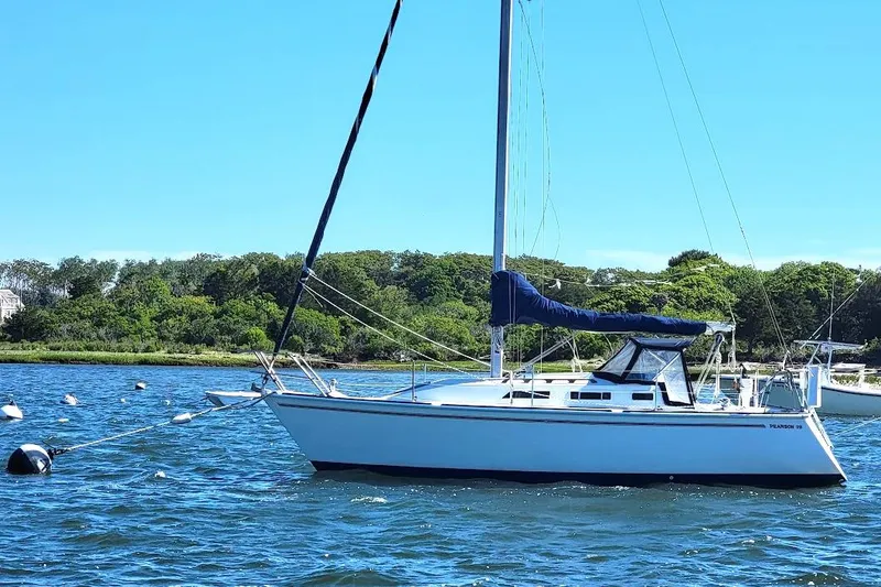 Slide: The Image of 1986 Pearson 28 sailboat anchored on a sunny day with lush green shoreline. - 27