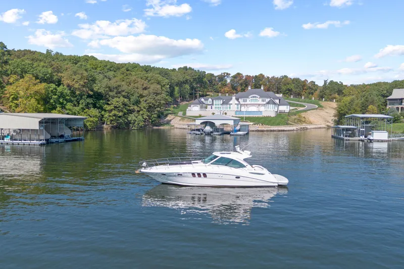 Slide: The Image of 2006 Sea Ray 48 Sundancer yacht on a serene lake with docks and luxury homes. - 11