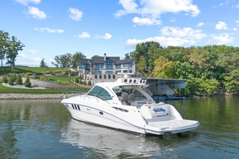 Slide: The Image of 2006 Sea Ray 48 Sundancer yacht on a serene lake near a luxurious waterfront home. - 2