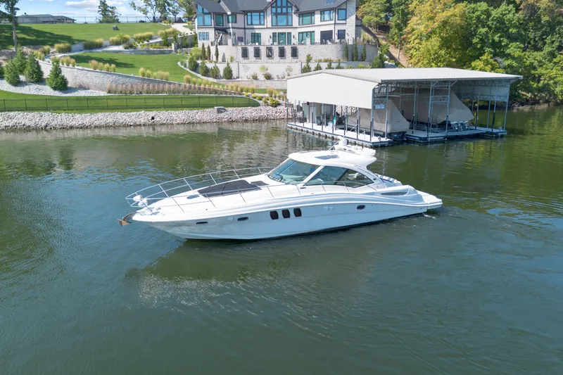 Slide: The Image of 2006 Sea Ray 48 Sundancer yacht cruising near a luxurious waterfront property. - 8