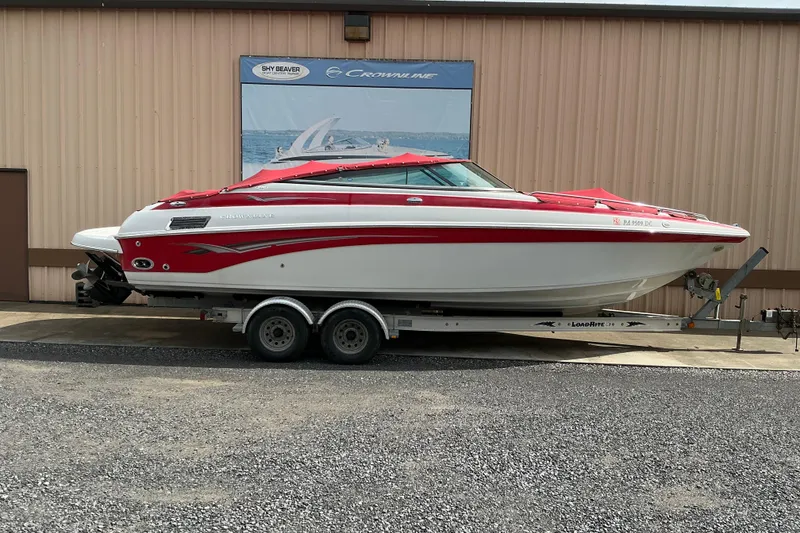 The Image of 2004 Crownline 270 BR boat on trailer, red and white design, parked outside a building. - 0