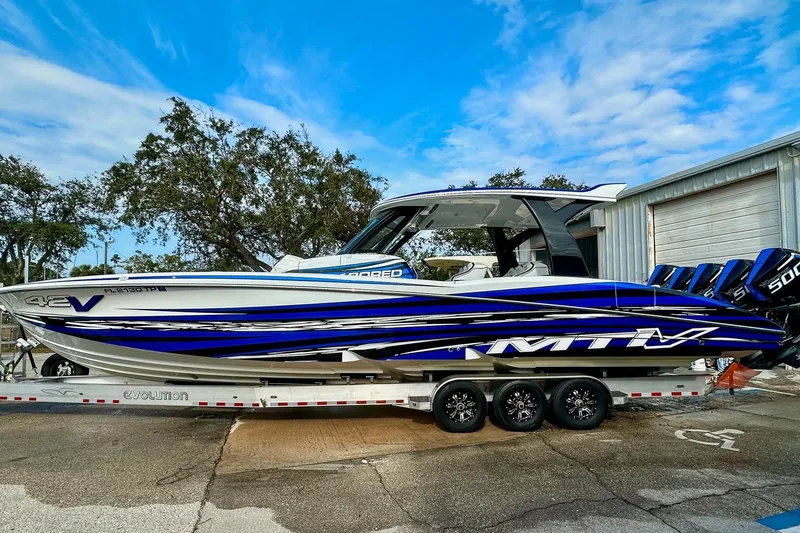 Slide: The Image of 2024 MTI V42 boat with blue and white design on a trailer, parked outdoors. - 22