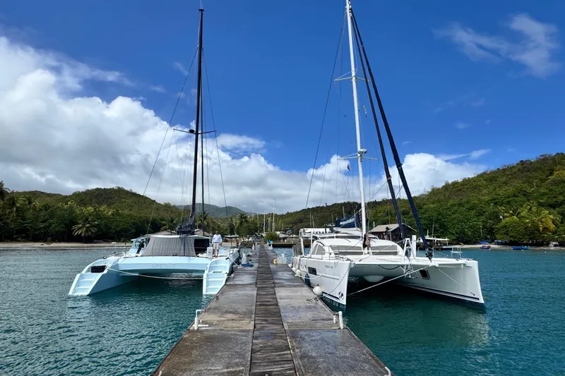 Slide: The Image of Two catamarans docked at a scenic marina, surrounded by lush green hills and blue skies. - 7