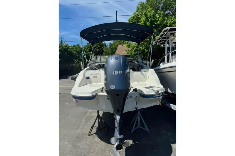 Slide: The Image of 2018 Stingray 201 DC boat with 150 HP engine, parked outdoors under blue sky. - 10