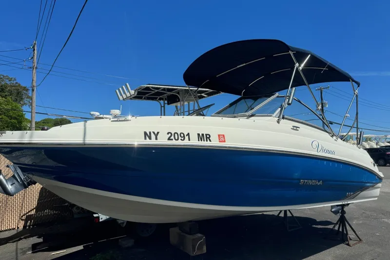 The Image of 2018 Stingray 201 DC boat with blue hull and canopy, docked on land. - 6