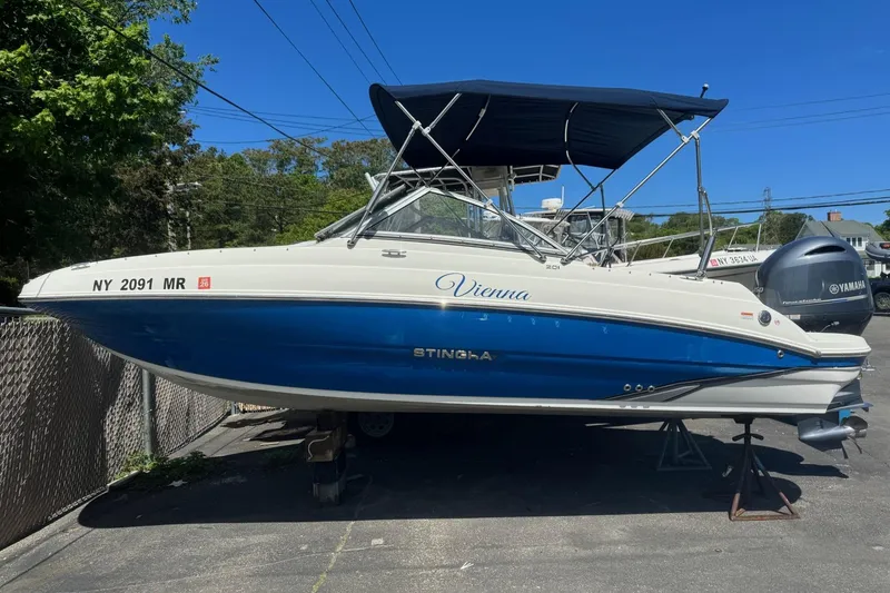 Slide: The Image of 2018 Stingray 201 DC boat with blue hull and canopy, parked on a trailer. - 9