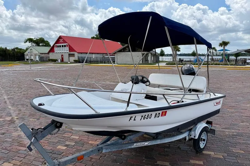 The Image of 2002 Boston Whaler 130 Sport boat on trailer with blue canopy, parked on brick pavement. - 1