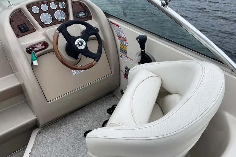 Slide: The Image of 2004 Sea Ray 240 Sundancer helm with steering wheel and white captain's chair. - 13