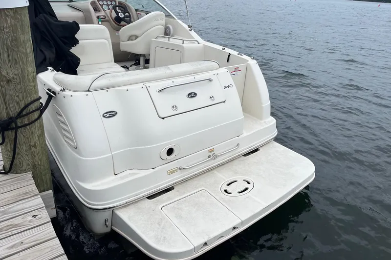 Slide: The Image of 2004 Sea Ray 240 Sundancer boat docked by the water, showcasing its rear deck and seating. - 6