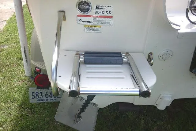 Slide: The Image of 2013 Carolina Skiff 198 DLV boat ladder and platform, featuring safety stickers and trailer license plate. - 21