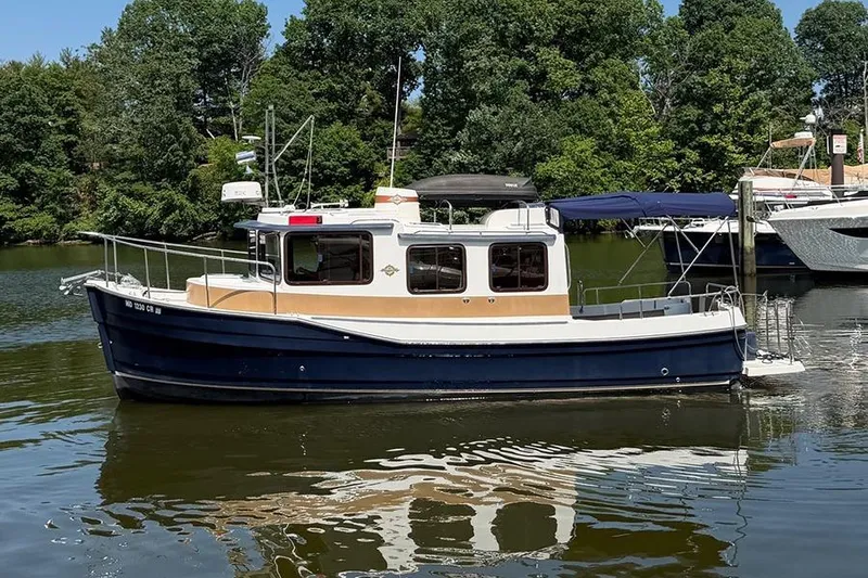 The Image of 2016 Ranger Tugs R-27 boat on a calm lake with lush green trees. - 1