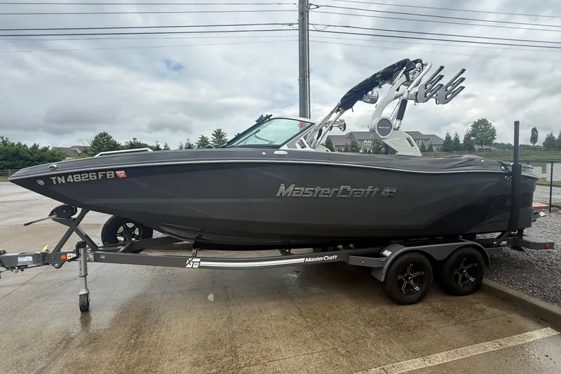 Slide: The Image of 2021 MasterCraft XT22 boat on trailer, parked outdoors on a cloudy day. - 2