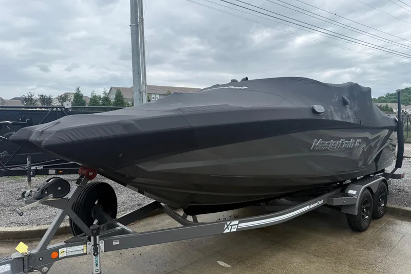 Slide: The Image of 2021 MasterCraft XT22 boat covered on trailer, parked outdoors under cloudy sky. - 6