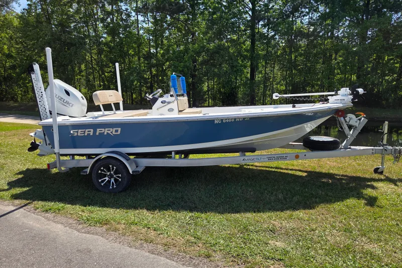 The Image of 2024 Sea Pro 172 Bay boat on trailer, parked on grass, surrounded by trees. - 0