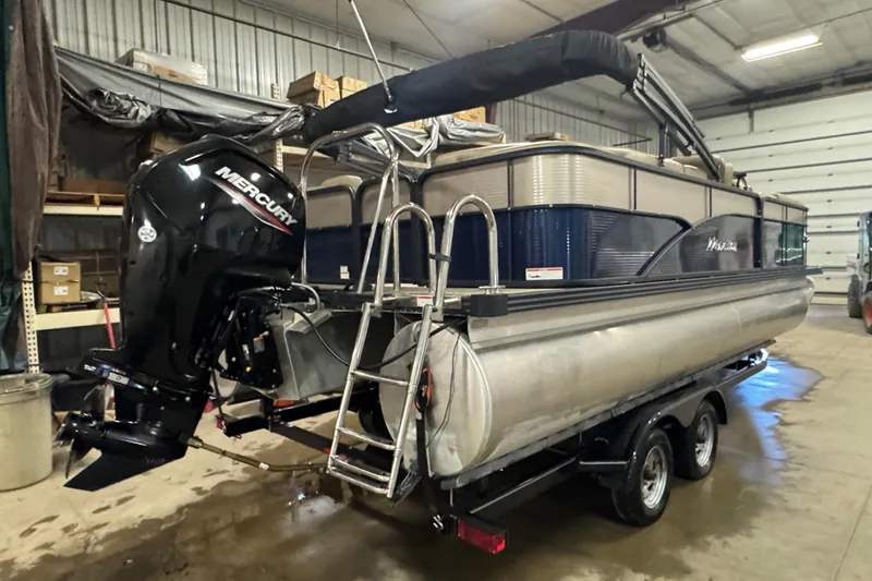 Slide: The Image of 2021 Manitou 22 Aurora LE Standard pontoon boat with Mercury outboard motor in a garage. - 3