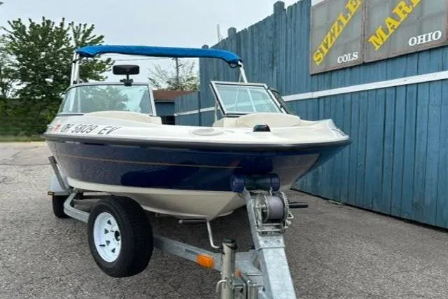 Slide: The Image of 2010 Bayliner 175 Bowrider on trailer, parked near blue fence at marina. - 2