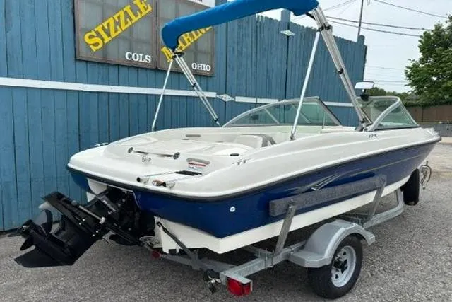 Slide: The Image of 2010 Bayliner 175 Bowrider boat on trailer, blue and white, parked near blue building. - 4