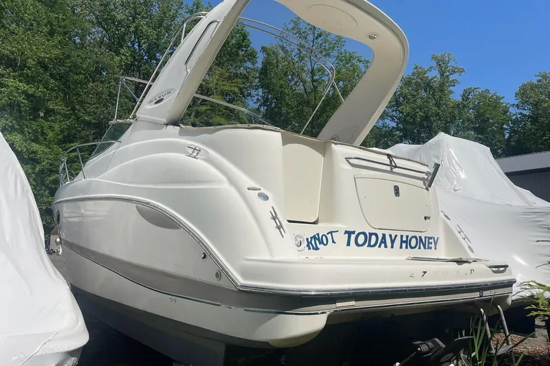 Slide: The Image of 2002 Maxum 2700 SCR boat named "Knot Today Honey" in storage, surrounded by trees. - 2