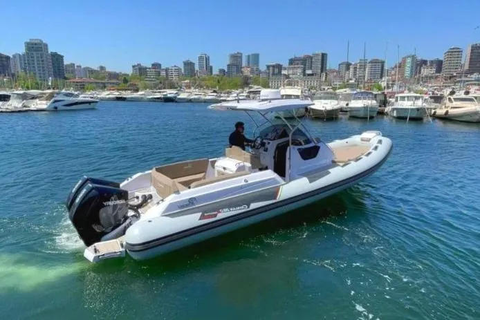 Slide: The Image of 2025 Ranieri CAYMAN 28 EXECUTIVE boat cruising in a marina with city skyline in the background. - 1