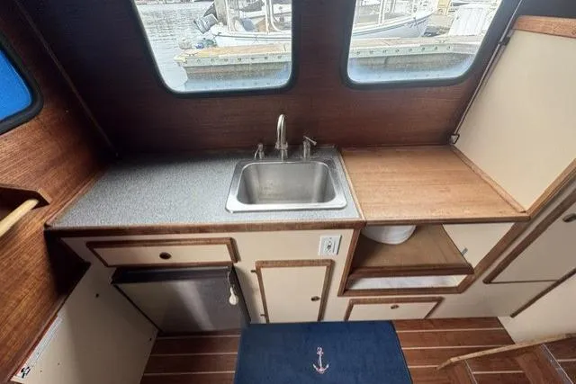 Slide: The Image of Interior of a 1983 Nordic Tug 26, featuring a compact kitchen with sink and wooden cabinetry. - 11